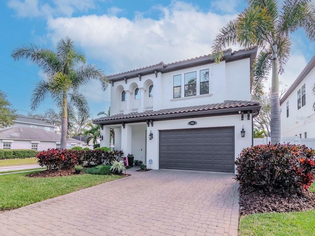 mediterranean / spanish home with a garage, a tiled roof, decorative driveway, and stucco siding