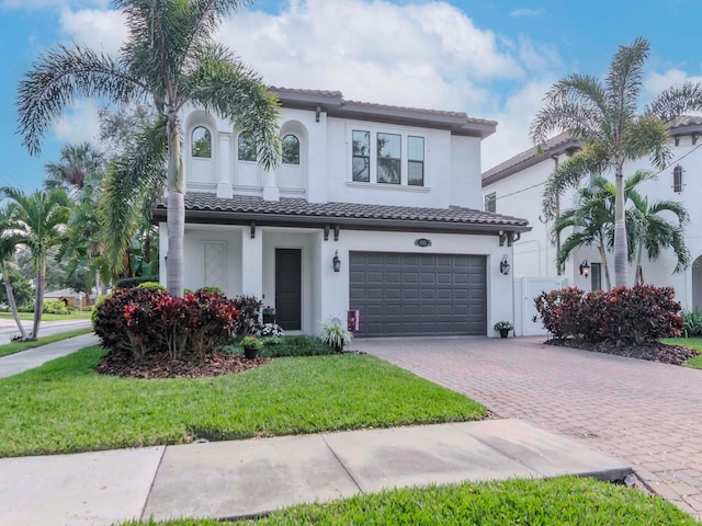 mediterranean / spanish home featuring decorative driveway, an attached garage, a tile roof, and stucco siding