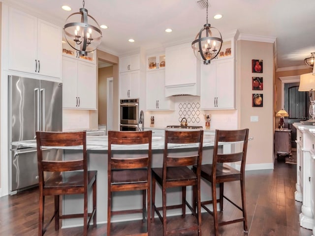 kitchen with stainless steel appliances, a center island with sink, white cabinetry, and decorative light fixtures