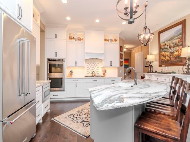 kitchen featuring stainless steel appliances, a kitchen island with sink, glass insert cabinets, and white cabinetry