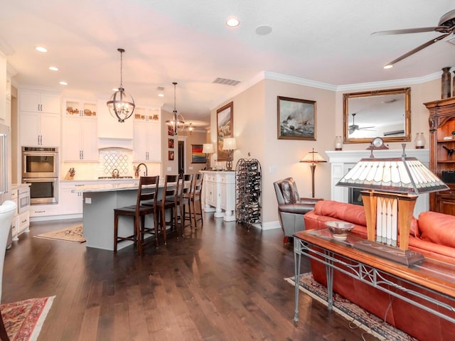 kitchen with white cabinets, decorative light fixtures, a kitchen island with sink, light countertops, and double oven