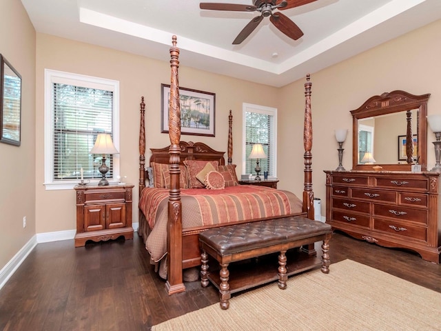 bedroom featuring a tray ceiling, dark wood-style flooring, and baseboards
