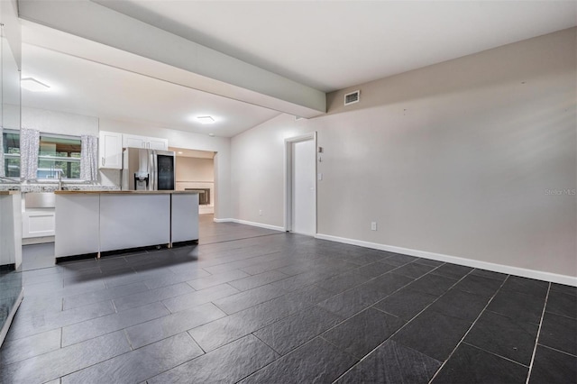 unfurnished living room with baseboards, visible vents, and beam ceiling