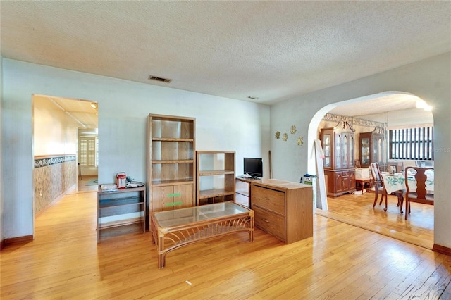 living room with arched walkways, a textured ceiling, light wood-type flooring, and visible vents