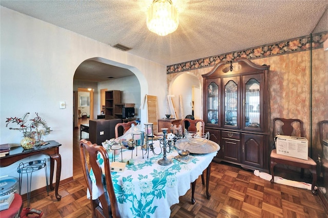 dining space with baseboards, visible vents, arched walkways, and a textured ceiling