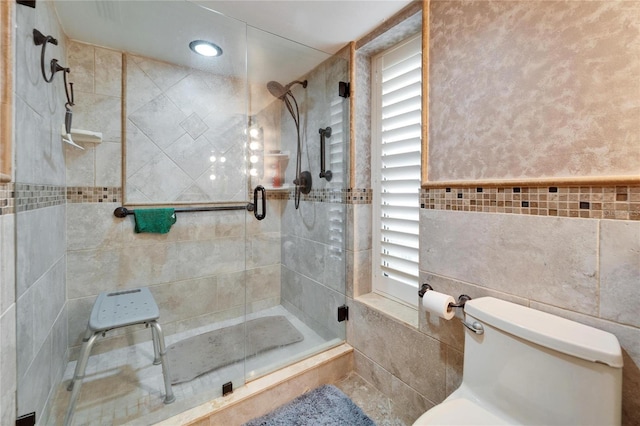 full bath with toilet, a wainscoted wall, a shower stall, and tile walls