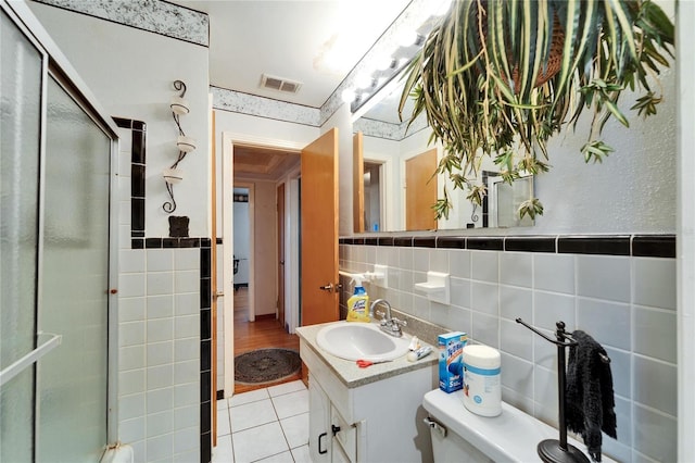 full bath featuring tile patterned flooring, visible vents, vanity, tile walls, and a shower with door