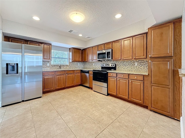 kitchen featuring light stone counters, a sink, visible vents, appliances with stainless steel finishes, and brown cabinetry