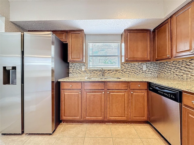 kitchen with light tile patterned floors, appliances with stainless steel finishes, brown cabinetry, a sink, and light stone countertops