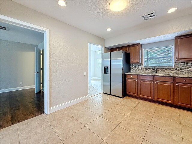 kitchen with visible vents, decorative backsplash, a sink, light stone countertops, and stainless steel fridge with ice dispenser