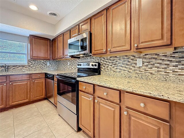 kitchen featuring appliances with stainless steel finishes, brown cabinets, a sink, and light tile patterned flooring