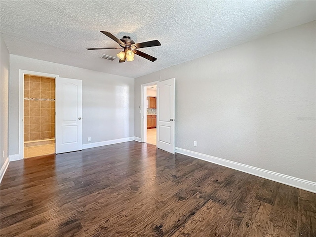 unfurnished bedroom with a textured ceiling, dark wood-style flooring, ensuite bathroom, and baseboards