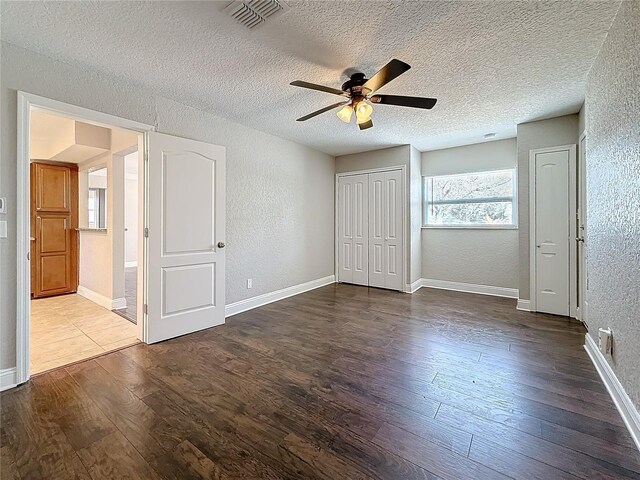 unfurnished bedroom with a textured ceiling, a textured wall, wood finished floors, visible vents, and baseboards