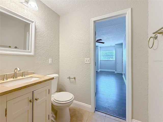 half bath featuring a textured ceiling, a textured wall, tile patterned flooring, toilet, and vanity