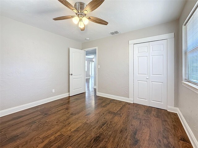 unfurnished bedroom with a textured wall, dark wood-type flooring, visible vents, and baseboards