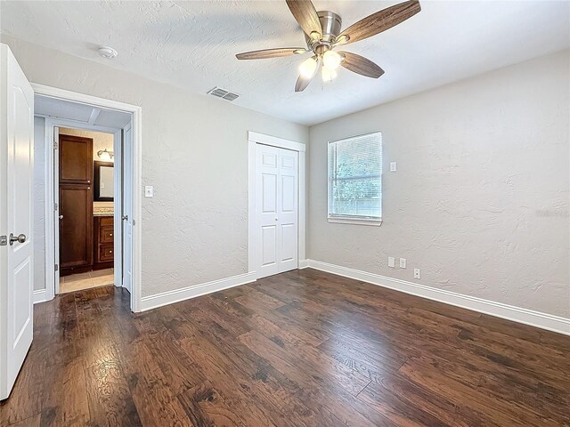 unfurnished bedroom with baseboards, visible vents, dark wood-style flooring, and a textured wall