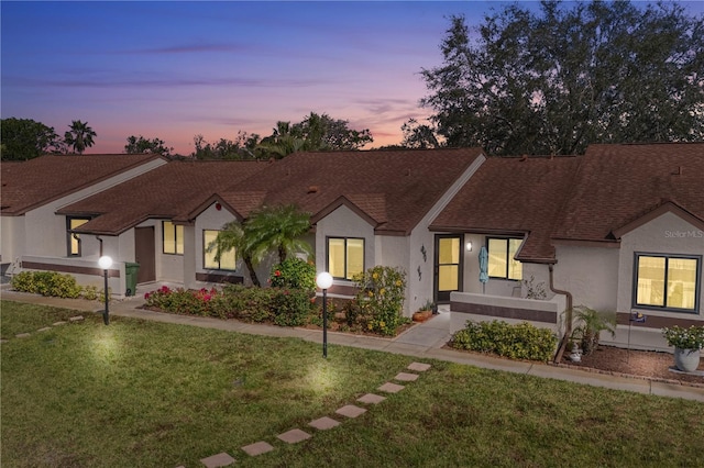 view of front facade with roof with shingles, a lawn, and stucco siding