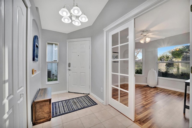 foyer entrance featuring vaulted ceiling, light tile patterned floors, ceiling fan with notable chandelier, and baseboards