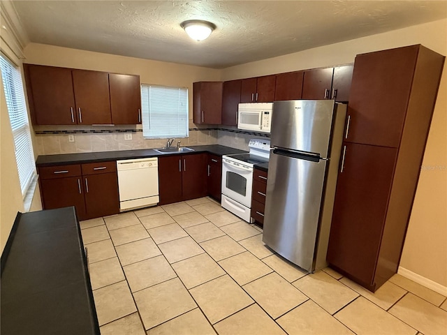 kitchen with white appliances, dark countertops, a sink, and a wealth of natural light