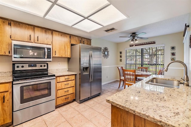 kitchen featuring appliances with stainless steel finishes, brown cabinetry, light tile patterned flooring, and a sink