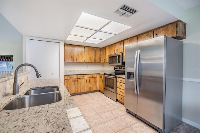 kitchen featuring stainless steel appliances, visible vents, brown cabinetry, a sink, and light stone countertops