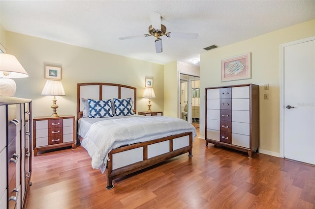 bedroom with a textured ceiling, ceiling fan, connected bathroom, wood finished floors, and visible vents