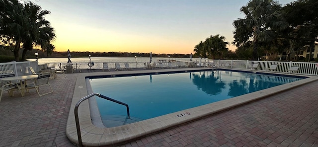 pool at dusk with a patio, fence, and a community pool