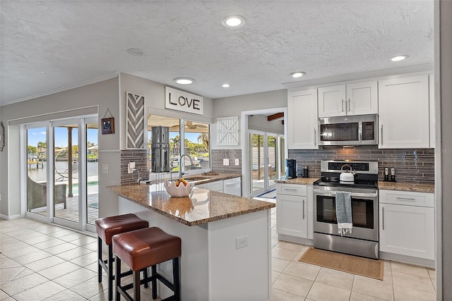 kitchen featuring a breakfast bar, stainless steel appliances, white cabinets, light stone countertops, and a peninsula