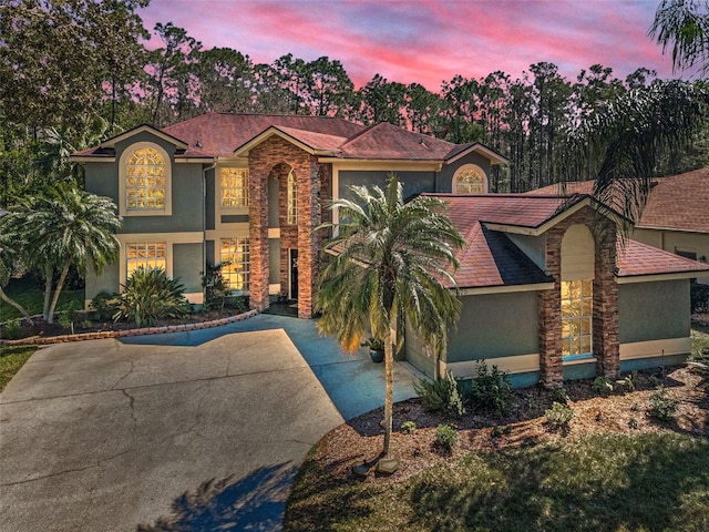 mediterranean / spanish home featuring an attached garage, driveway, stone siding, and stucco siding