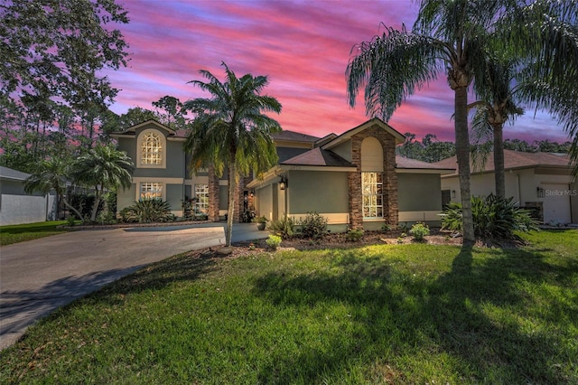 mediterranean / spanish house featuring stucco siding, concrete driveway, an attached garage, stone siding, and a front lawn