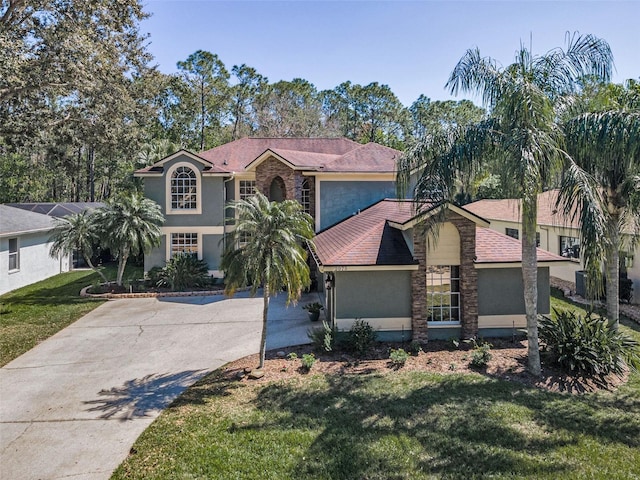 view of front facade with stucco siding, stone siding, concrete driveway, and a front yard