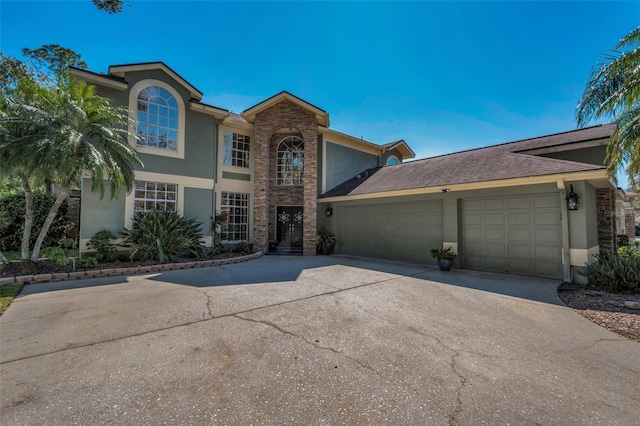 traditional home featuring a garage, stone siding, driveway, and stucco siding