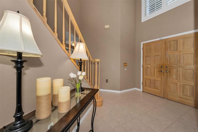 foyer entrance with stairs, light tile patterned flooring, a towering ceiling, and baseboards