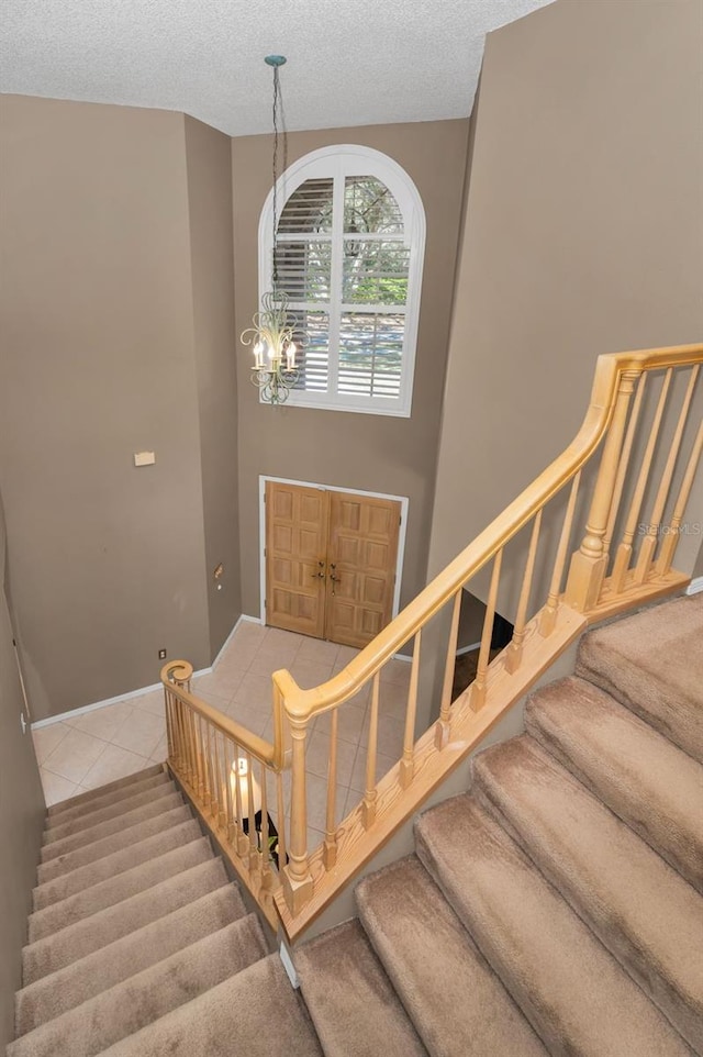 stairway with a textured ceiling, tile patterned floors, and a notable chandelier