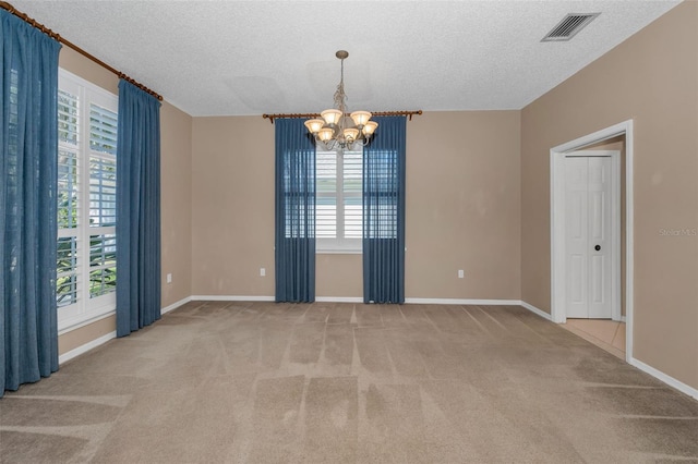 carpeted spare room featuring baseboards, visible vents, a chandelier, and a textured ceiling