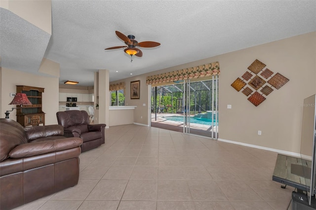 living area with a ceiling fan, a sunroom, light tile patterned flooring, a textured ceiling, and baseboards