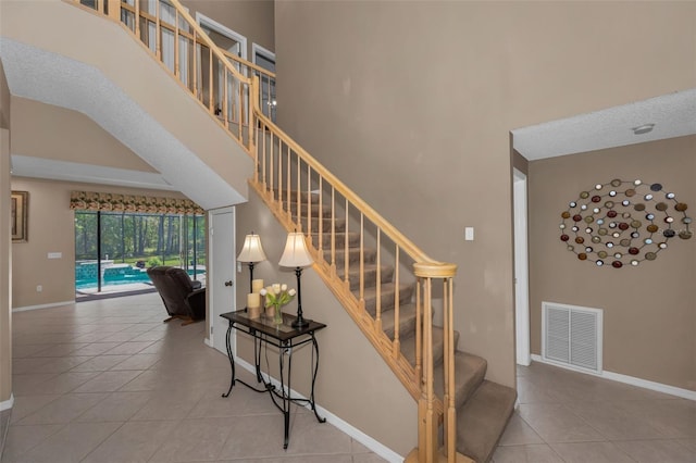 staircase featuring baseboards, a towering ceiling, visible vents, and tile patterned floors