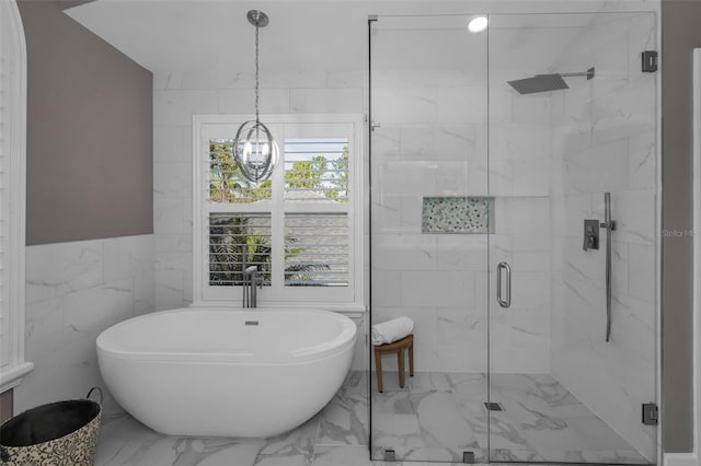 bathroom featuring marble finish floor, a notable chandelier, tile walls, a marble finish shower, and a freestanding bath