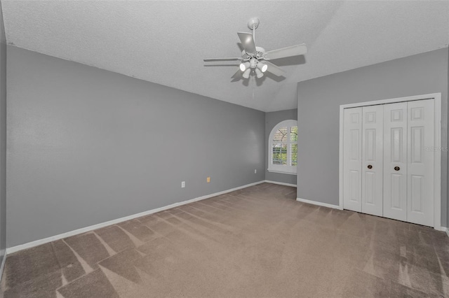 unfurnished bedroom with a textured ceiling, carpet, lofted ceiling, and baseboards