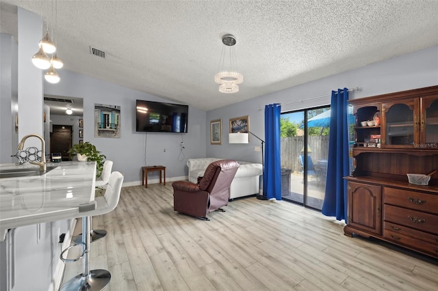 living area with lofted ceiling, a textured ceiling, visible vents, baseboards, and light wood finished floors