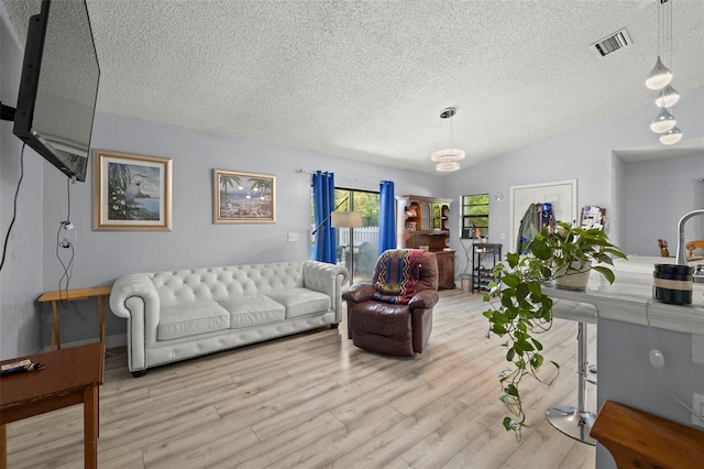 living room featuring lofted ceiling, light wood finished floors, a textured ceiling, and visible vents