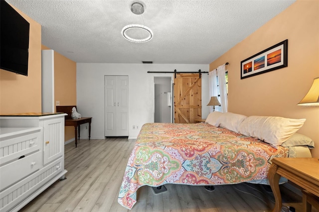 bedroom with a textured ceiling, light wood finished floors, and a barn door