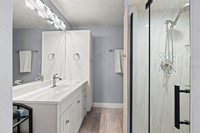 full bath with a stall shower, baseboards, vanity, and a textured ceiling