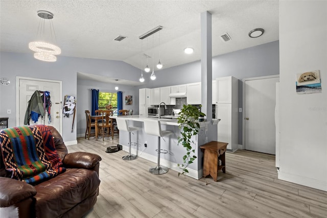 living area featuring light wood-type flooring, lofted ceiling, visible vents, and a textured ceiling