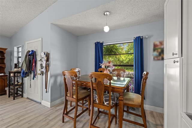 dining area with lofted ceiling, light wood-style flooring, baseboards, and a textured ceiling