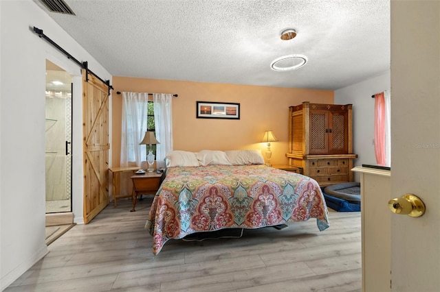 bedroom featuring light wood-style floors, a barn door, visible vents, and a textured ceiling