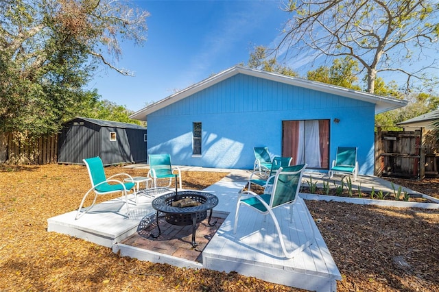 rear view of house featuring an outbuilding, a shed, an outdoor fire pit, and fence