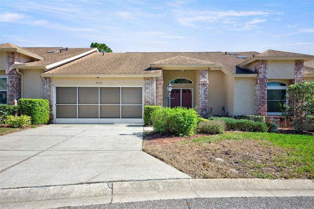 view of front of house with driveway, brick siding, roof with shingles, an attached garage, and stucco siding