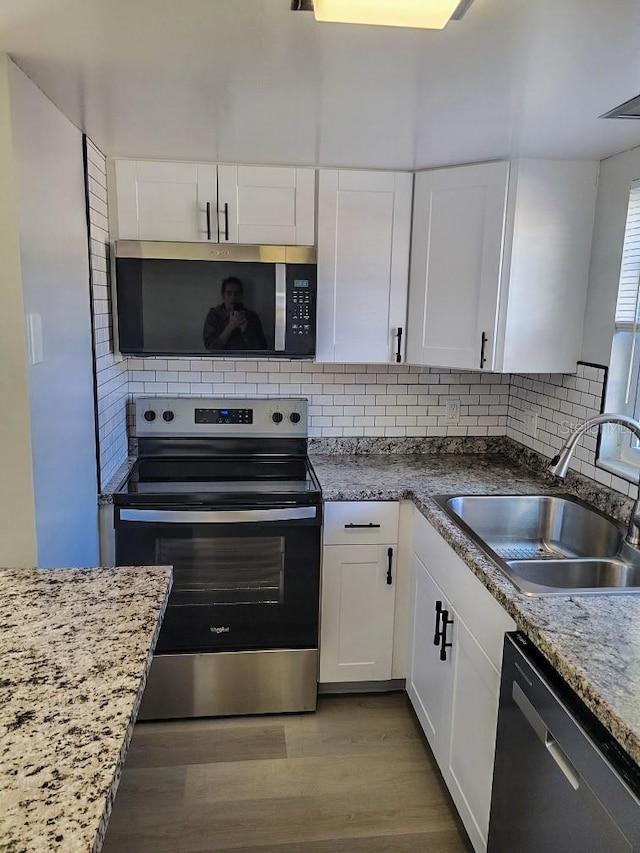 kitchen with stainless steel appliances, tasteful backsplash, a sink, and white cabinets