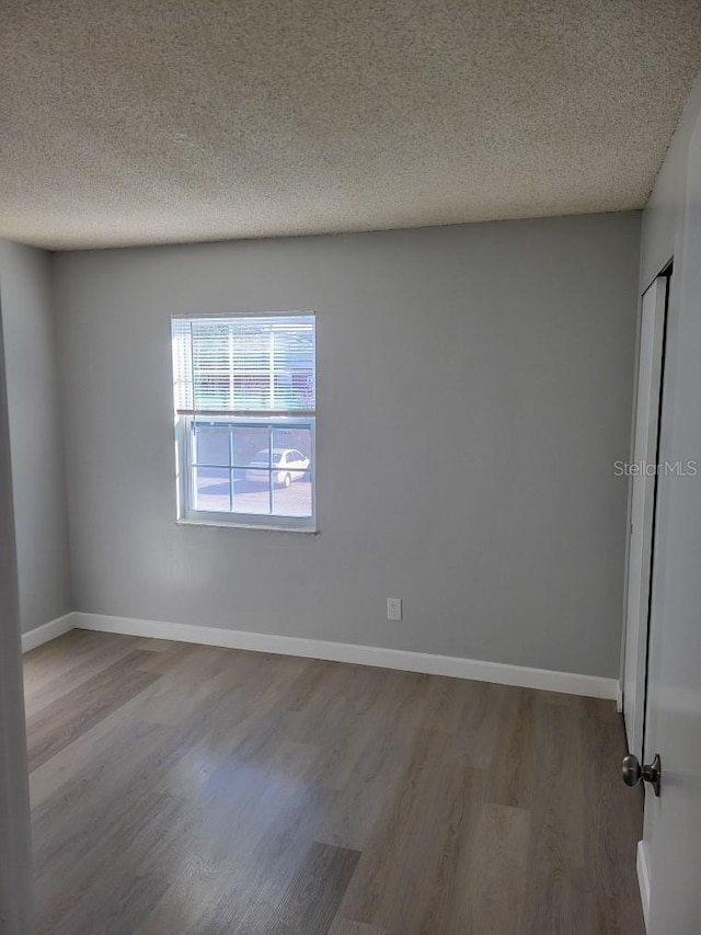 spare room featuring a textured ceiling, baseboards, and wood finished floors